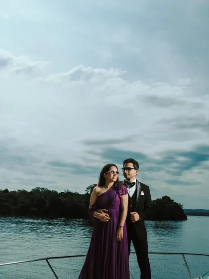 A stylish portrait of a couple dressed in formal wear on a yacht. The dramatic sky and open water provide a sophisticated and powerful backdrop for this pre-wedding photo.