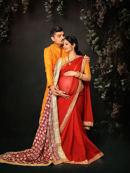 A stunning portrait of an expecting couple in traditional Indian attire. The rich red and gold of the saree and the vibrant yellow of the kurta create a visually splendid and culturally rich image.