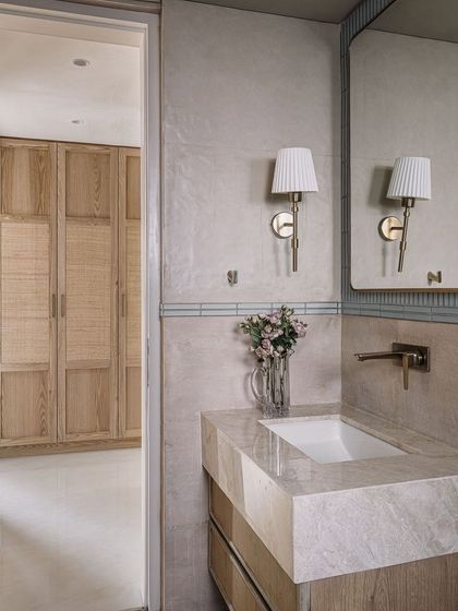 A bathroom in Eden House featuring a marble vanity and classic wall sconces, with a view into a closet with natural wood and cane doors.