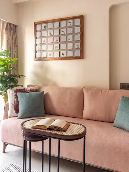 This cozy living room corner uses a blush pink sofa and green accents to feel spacious and serene. The hand-painted tile art piece adds a touch of elegance.