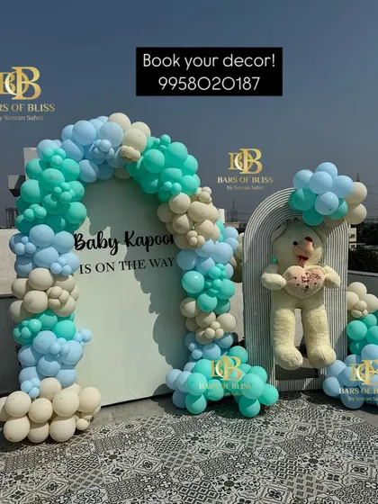 A full view of the 'Baby Kapoor is on the way' baby shower decor. The rooftop setting provides a beautiful backdrop for the balloon arch and personalized signage, creating a perfect photo spot.