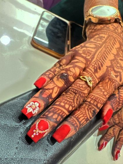 A bold and beautiful bridal set. The vibrant red nails are adorned with intricate 3D floral designs and pearl accents, creating a look that is both traditional and glamorous.
