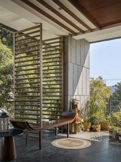 This wide, shaded verandah acts as an outdoor living room, furnished for comfort and surrounded by greenery. The louvered screens provide privacy and filter the sunlight, creating a perfect space for relaxation.