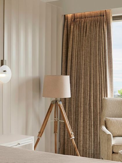 A comfortable armchair and ottoman by the window create a cozy reading nook for the couple to unwind in their spacious master bedroom.