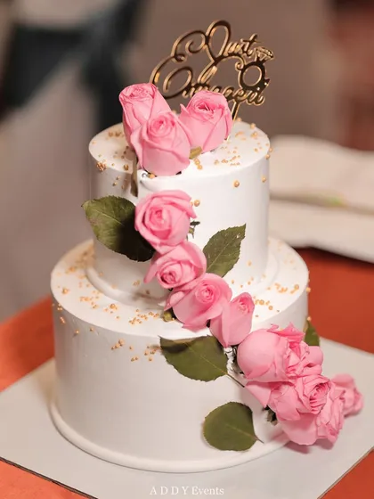 A beautiful two-tiered engagement cake, decorated with a cascade of fresh pink roses and a custom "Just Engaged" topper.