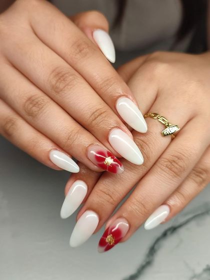 A simple yet beautiful design. These milky white almond nails are accented with a translucent red floral design and gold flakes.