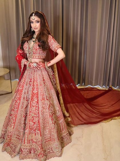 A full-length shot of a bride in a magnificent red lehenga. The makeup is glamorous yet classic, designed to make her feel like royalty on her big day.