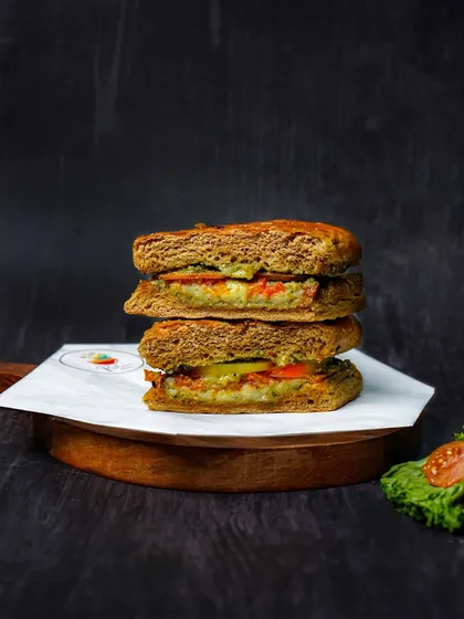 A pesto sandwich cut in half and stacked, with a hint of fresh lettuce and tomato on the side. The dark, rustic styling is perfect for a cafe's social media feed.