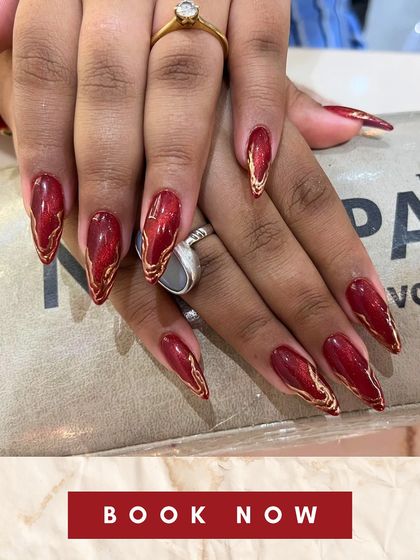 A close-up of fiery red stiletto extensions with intricate gold accents. This image highlights the sharp, clean shape and artistic detail I can achieve with sculpted extensions.