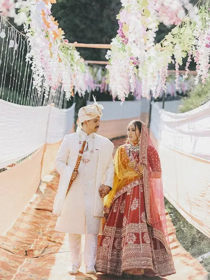 A classic wedding day portrait of the couple walking hand-in-hand under a beautiful floral canopy. This shot captures the grandeur and romance of the wedding ceremony entrance.