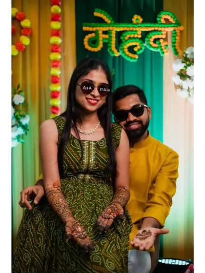 A fun and quirky photo of the couple wearing matching sunglasses, showing off their mehendi-adorned hands.