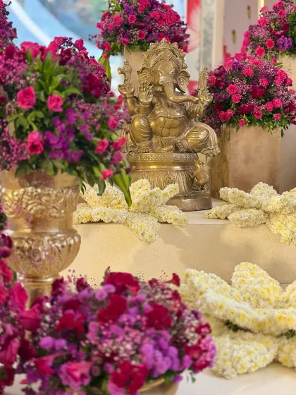 When the welcome is equal parts grand, traditional, and auspicious. A brass Ganesha idol is surrounded by a sea of vibrant magenta and purple flowers. ✨