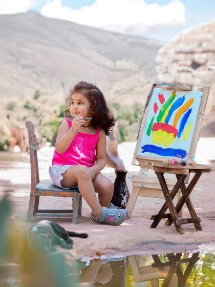 A young artist deep in thought, painting a masterpiece against a stunning mountain backdrop. This creative shoot combines a fun activity with a beautiful location.