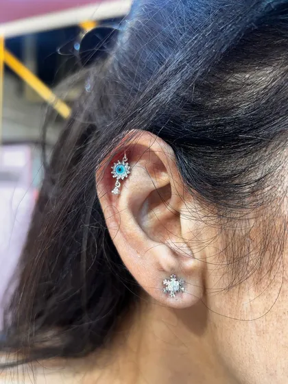 An evil eye hanging from the helix piercing offers both style and protection. Paired with a simple snowflake stud, it creates a unique and meaningful combination.