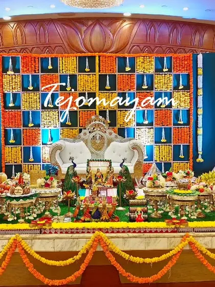 A baby shower setup with a colorful checkered backdrop and peacock figures. The plate decoration is elaborate and full of traditional elements.