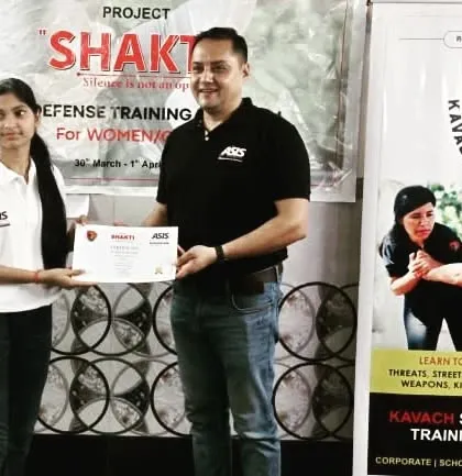 A participant receiving her certificate in front of the Kavach and Project 'Shakti' banners.