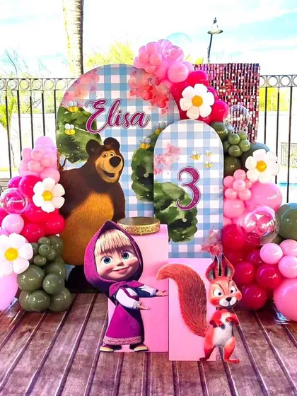 An outdoor Masha and the Bear themed third birthday party. This detailed setup includes character cutouts and balloon arrangements in a rustic, woodland style.
