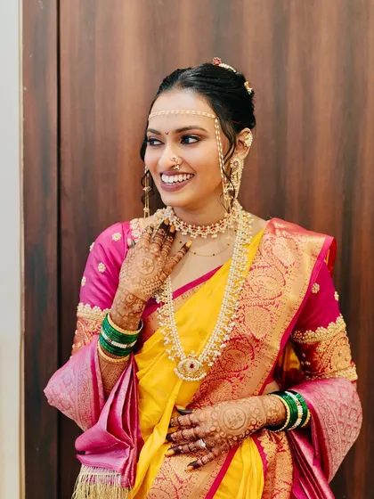A candid shot capturing the bride's joy. The rose gold eyeshadow and traditional jewelry add a touch of modern elegance to her classic Marathi look.