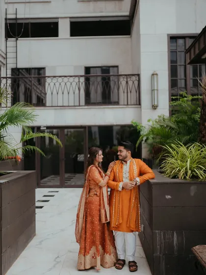 The couple shares a quiet moment together outdoors, their traditional orange outfits glowing in the soft light.