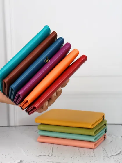 A hand holding a fan of our colorful passport organizers, demonstrating the wide range of shades we offer.