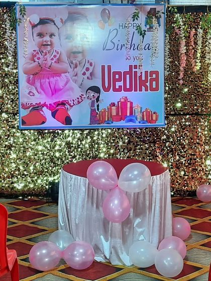A personalized birthday setup with a large photo banner of the birthday girl, Vedika. The sequin backdrop and simple balloon decor make the banner stand out.