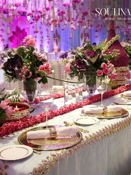 An opulent wedding table setting with a long floral runner and gold-rimmed plates, showcasing our flair for traditional yet grand decor.