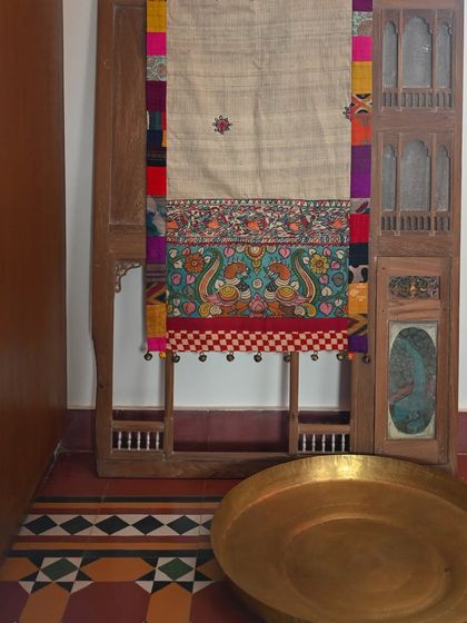A custom-made runner that combines Kalamkari and Madhubani art forms. The body is raw silk, bordered with a patchwork of scrap fabrics and finished with bell trims.