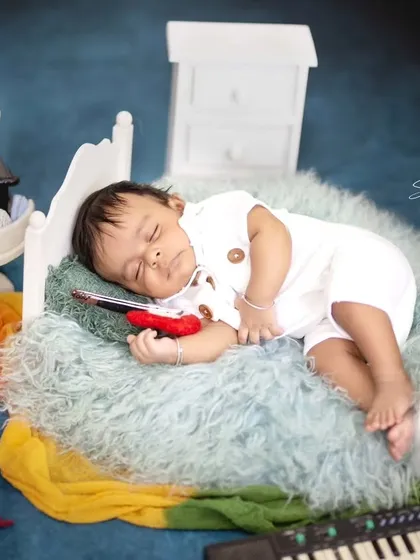 Dreaming of melodies. This baby is sleeping peacefully on a tiny bed, surrounded by musical props like a gramophone and keyboard.