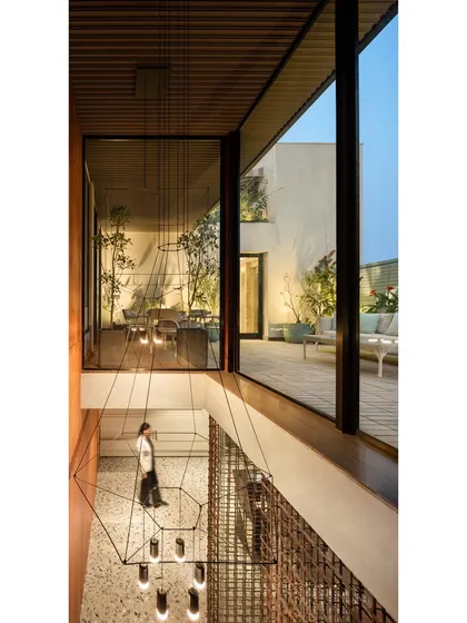 A view from the upper level of a double-height executive area, looking down past a minimal chandelier towards the terrace. This design choice was deliberate to create a sense of grandeur and connect the interior space with the outdoor oasis, enhancing the feeling of luxury and openness.
