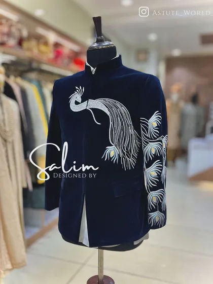 A mannequin displaying a navy blue velvet Jodhpuri jacket with a silver embroidered peacock. The design is elegant and symbolic, perfect for a wedding ceremony.