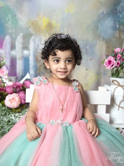 A full portrait of a toddler in a beautiful pink and green gown, sitting elegantly in a painted garden scene.