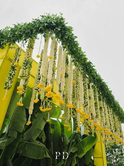 A beautiful floral installation for a Haldi, with hanging garlands of tuberose and marigolds against a bright yellow backdrop and banana leaves.