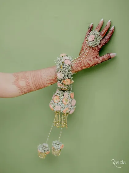 A detail shot of the bride's floral hand jewelry against a simple green wall, highlighting the intricate craftsmanship.