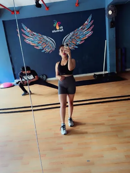 The gym is a place for focus and transformation. Here's a member taking a moment to capture her progress while another stretches in the background.