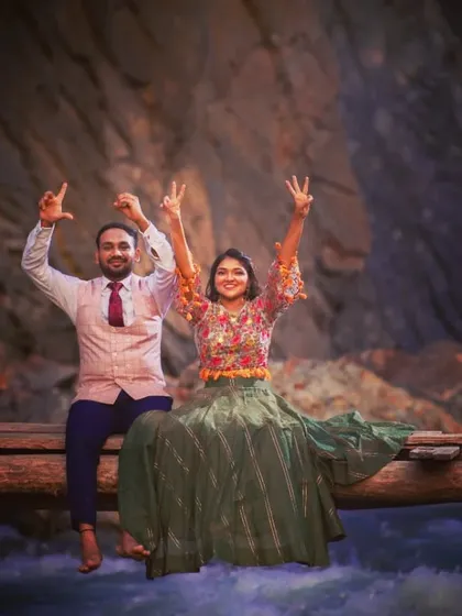 A fun and energetic shot of a couple on a wooden bridge over a flowing river, showing their playful side.