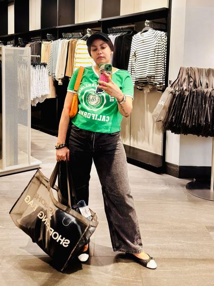 Another mirror selfie capturing the full casual ensemble. The combination of the graphic tee, wide-leg jeans, and cap creates a cool, laid-back look.