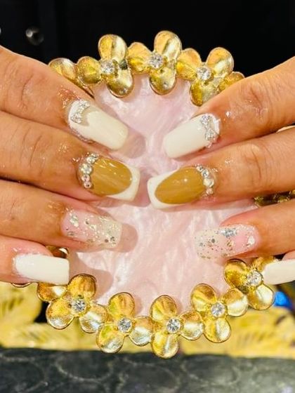 A unique design mixing solid white and mustard yellow nails with glitter and rhinestone accents.