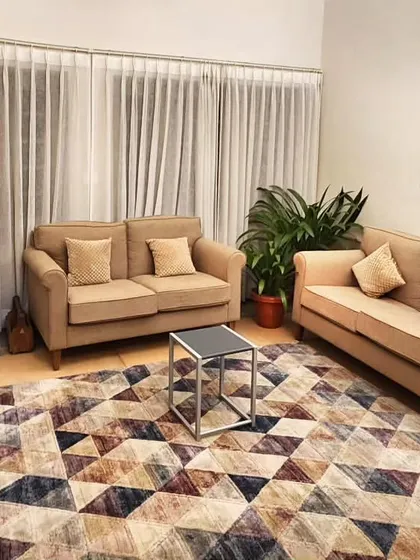 In this South Delhi bungalow with tall ceilings and original terrazzo floors, we introduced color and texture with a geometric rug. The neutral furniture palette allows the rug and the large traditional artwork to become the focal points, creating a cozy yet modern drawing room.