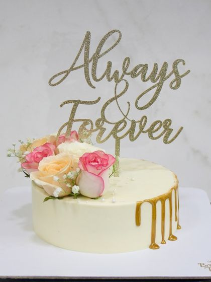 A simple and sweet anniversary cake with a golden drip, fresh flowers, and a beautiful "Always & Forever" topper. It's the perfect way to celebrate your love story.