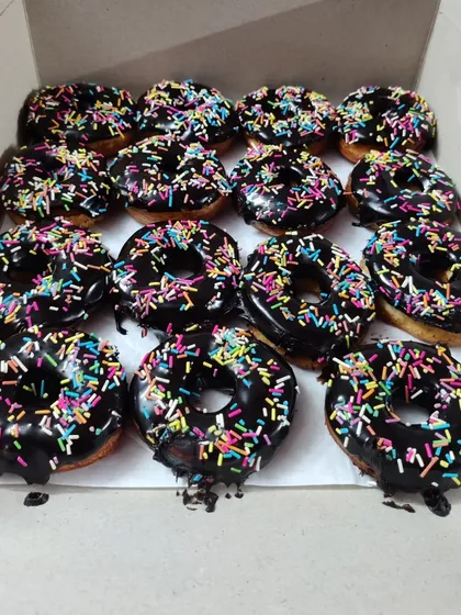 A big box of my classic chocolate donuts, perfect for sharing at the office or a party. Each one is dipped in a rich chocolate glaze and covered in colorful rainbow sprinkles.
