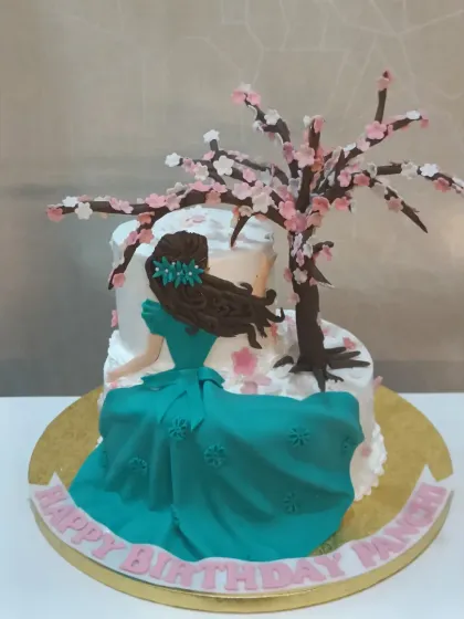 A serene and artistic cake featuring a fondant figure of a woman sitting under a delicate, handcrafted cherry blossom tree.