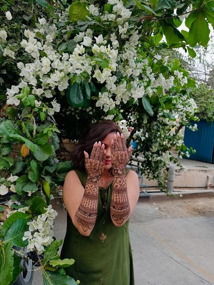Another lovely shot of a bride displaying her full-arm mehndi against a backdrop of white flowers.