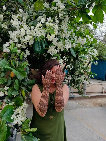 A beautiful client surrounded by flowers, her hands adorned with my intricate henna work. A perfect picture of festive grace.