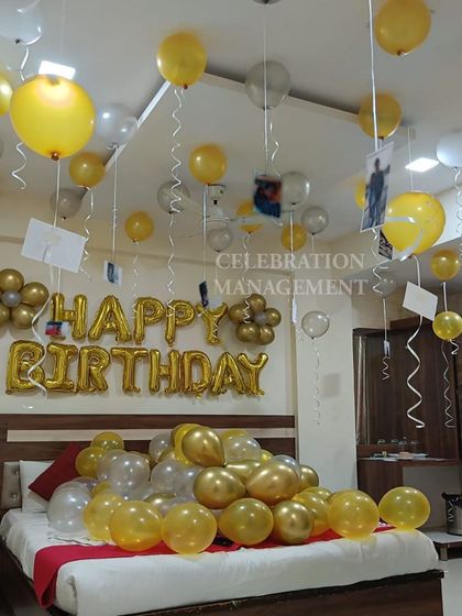 A simple and happy birthday room surprise. The bed is filled with gold and silver balloons, with more floating on the ceiling with photos attached, and a 'Happy Birthday' foil banner on the wall.