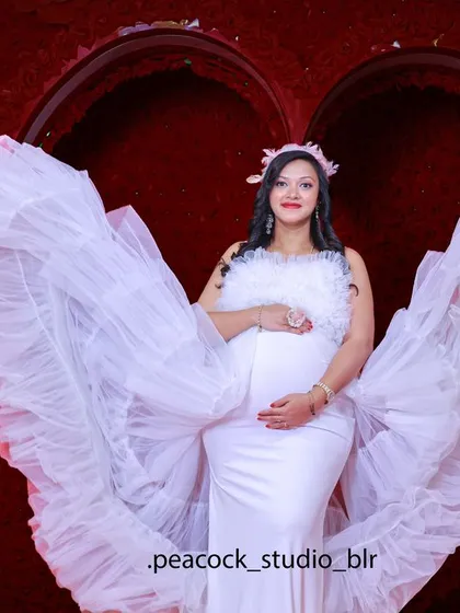 An angelic maternity portrait featuring one of my popular white gowns with dramatic wing-like sleeves, set against a romantic red floral heart in my studio.