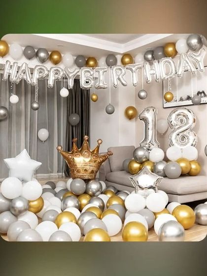 An 18th birthday room decoration in gold, silver, and white, with a large crown foil balloon.
