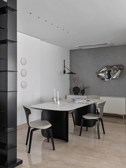 This dining area corner is an exercise in minimal precision. The textured grey wall provides a dramatic backdrop for a metallic, abstract wall sculpture, turning the dining experience into an encounter with art.