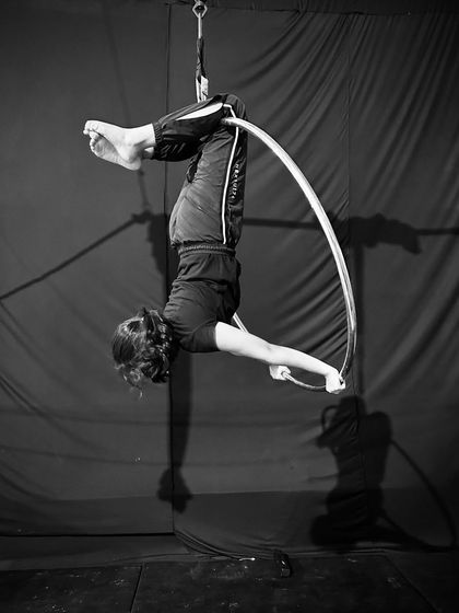 A black and white shot of a student in an inverted tuck position, highlighting the strength and form required for aerial hoop skills.