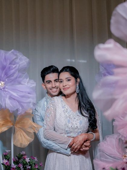 A happy, smiling portrait of the newly engaged couple. The whimsical paper flower backdrop adds a unique and modern touch to their photos.