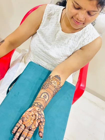 A happy client admiring her full-arm bridal mehendi. The design includes a Radha Krishna portrait on the palm and architectural motifs on the arm.